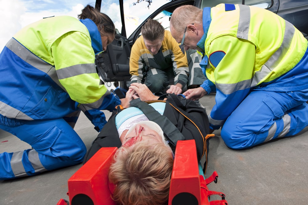 Paramedics and a fireman strapping a wounded woman with a neck brace on a stretcher