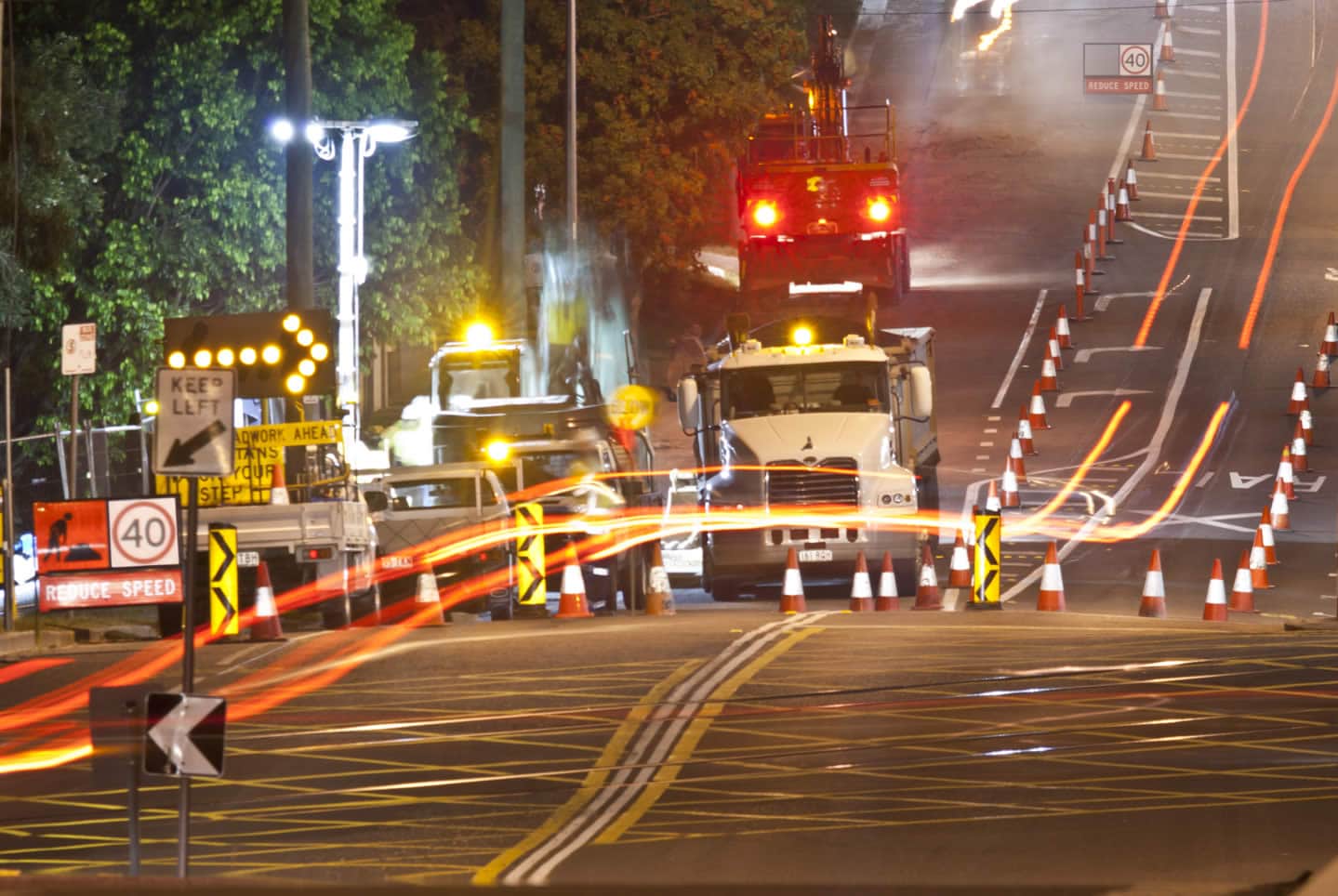 High-visibility roadwork zone with cones, signage, and construction vehicles at night, highlighting traffic management.